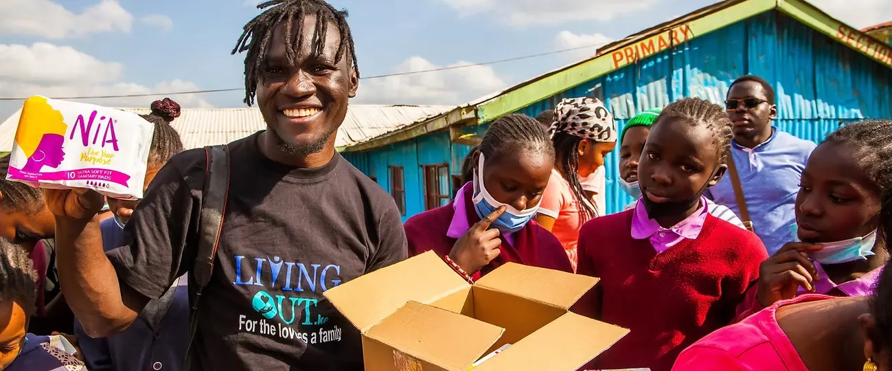 A Nawiri volunteer holding a pack of sanitary towels beside schoolgirls outside a primary school